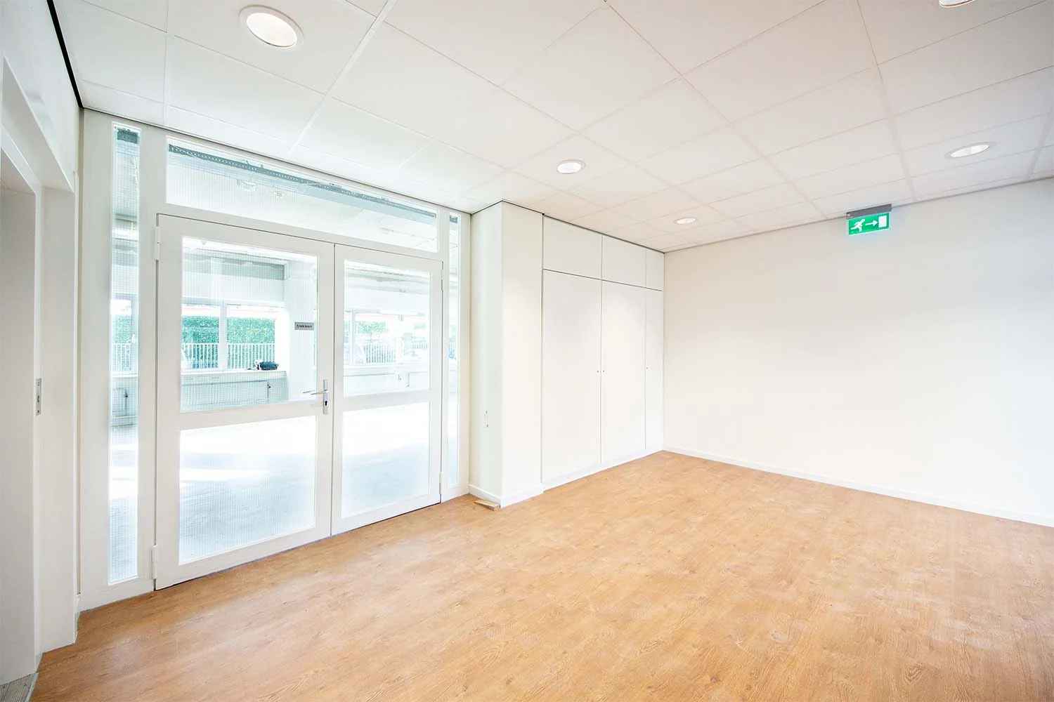 Lichte lege kamer met houten vloer, witte wanden, ingebouwde kasten en dubbele glazen deur aan de Huis-ter-Heideweg.